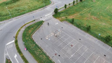 Piacenza, İtalya - 1 Ağustos 2025 Bir yol kavşağı yakınındaki boş bir otoparktan geçen bir motosikletlinin hava görüntüsünü yakalamak, şehir altyapısını ve dinamiklerini vurgulamak