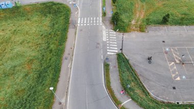 Piacenza, İtalya - 1 Ağustos 2025 İHA yaya geçitleri, bir otopark, sokak lambaları, yeşil alanlar ve bir yaz günü yürüyen ve bisiklete binen birkaç kişi ile boş bir kavşağı yakalıyor