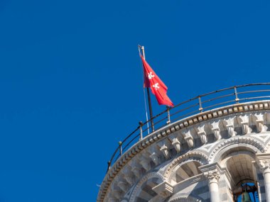 Pisa, Toskana - 16 Ekim 2025 Tuscany İtalya 'da Açık Mavi Gökyüzü Altındaki Tarihi Eğik Pisa Kulesi' nde Güneşli Bir Gün İkonik Tarihi Mimarisinde Kırmızı Bayrak Dalgaları Gururla Vuruyor
