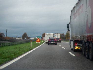 Brescia, İtalya 21 Kasım 2025 Yağmurlu bir kış trafiğinde Cremona yakınlarındaki İtalyan A21 otoyolunda trafik sıkışıklığı, uyarı işareti ve bulutlu gökyüzü