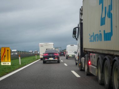 Brescia, İtalya 21 Kasım 2025 Bir çok şeritli otoyolda durgun bir trafik kuyruğunda, birleşme şeritleriyle ilgili bir uyarı levhasına yaklaşıyor. Yağmurlu ve bulutlu hava trafik sıkışıklığına yol açıyor
