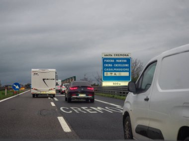 Brescia, İtalya 21 Kasım 2025 Cremona, Lombardy yakınlarındaki bir otoyol çıkışında trafik kuyruğu, arabalar ve bulutlu gökyüzü altında yavaş ilerleyen bir karavan.