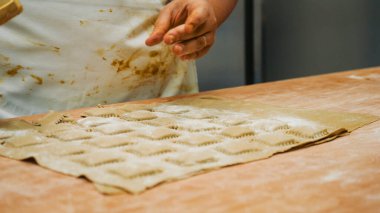 Ellerin ahşap bir masada el yapımı ravioli yaratması geleneksel İtalyan mutfağı için hamura makarna damgası basması otantik yemek hazırlığını vurguluyor.