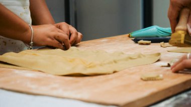 Çocuğun elleri ahşap bir yüzeyde taze bir hamur parçasını yoğurup şekillendiriyor, pişirme sanatını öğreniyor ve mutfak ortamında geleneksel hamur işleri yapıyor.