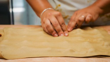 Çocuğun elleri ahşap bir yüzeyde taze bir hamur parçasını yoğurup şekillendiriyor, pişirme sanatını öğreniyor ve mutfak ortamında geleneksel hamur işleri yapıyor.