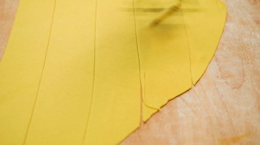 Taze makarna hamuru ahşap bir yüzeyde şeritler halinde kesilerek, ev yapımı İtalyan erişteleri ve aşçılık gelenekleri için dikkatli hazırlık sürecinin altını çiziyor.