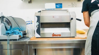 Piacenza, İtalya - 5 Eylül 2025 Profesyonel mutfak gereçleri ve paslanmaz çelik tezgahların üzerinde duran bir et dilimleyici, önlük giymiş bir şef taze makarna hazırlıyor.