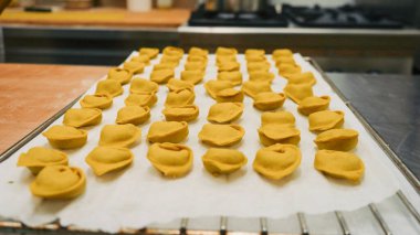 Şef uzmanca doldurulmuş taze makarna hazırlıyor, profesyonel bir mutfakta tortellini yaratıyor, sanatsal süreci ve geleneksel İtalyan yemek işçiliğini sergiliyor.