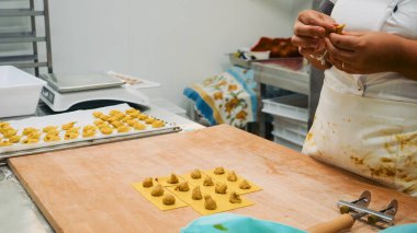 İki kadın ellerini titizlikle hamurdan taze tortellini ve ravioli hazırlayıp geleneksel İtalyan makarna üretiminin kalitesini ve hassasiyetini sağlamak için kullanıyor.