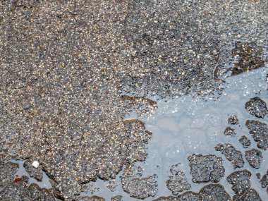 Dokulu koyu asfalt yüzeyi, yağmurdan sonra kısmen yansıtıcı bir su birikintisiyle kaplı.