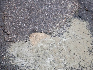 Yıpranmış kentsel asfalt kaldırımın detaylı görüntüsü çatlakları ve çürümeyi gösteren açık renkli desenli yamayı gösteriyor.