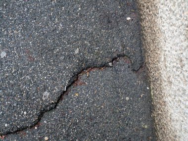 Belirtilen bir kırık, yıpranmış siyah granüler katran yüzeyinin yapısal uzlaşmayı ortaya koyan tek parça kalıbını bozar.