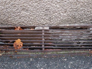 Yıpranmış bir metal yağmur giderine yakın çekim. Sonbahar yapraklarıyla dolu dokulu bir şehir yüzeyine ızgara yap.