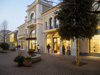 Fidenza, İtalya 6 Aralık 2025 Fidenza Village, İtalyan lüks moda mağazası, akşamları Noel alışverişi sırasında butikleri ve ağaçları ışıklandırıyor.