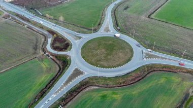 Çağdaş dairesel kavşağın hava aracı görüntüsü ve açık bir gökyüzü altında yeşil tarım alanlarından geçen yolları bağlayan kırsal ulaşım altyapısı ve trafik
