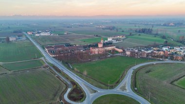 Kutsal Bakire Merhamet Mabedi ve SP415 Strada Paullese, Lombardy, İtalya boyunca uzanan günbatımı altın saatinde tarımsal tarlaları ve Alpleri olan modern bir kavşak.