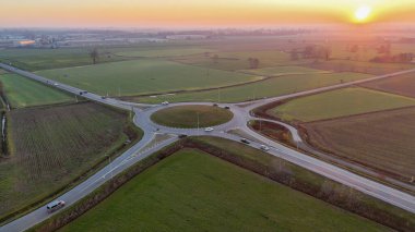 Altın saatinde yeşil tarlalardan geçen modern bir döner kavşağın hava manzarası, sakin kırsal altyapı ve yollar Paullese yakınlarındaki İtalyan kırsalında zikzak çiziyor.