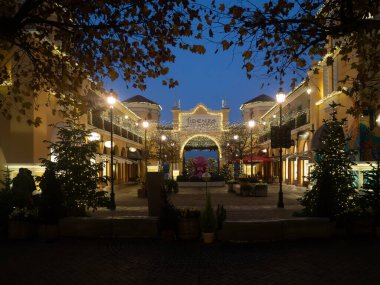 Fidenza, İtalya 5 Aralık 2025 alacakaranlıkta Fidenza Köyü, festival dekorasyonları, Noel ağaçları ve lüks moda butikleri aydınlatarak eşsiz bir alışveriş deneyimi sunuyor.