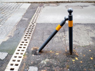 Çürümeyi ve bakımsızlığı gösteren dik bir direğin yanındaki kırık kaldırıma eğilmiş ağır hasarlı bir şehir kordonu.