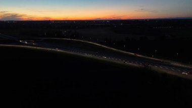 Gece hava görüntüsü A21 otoyolu Piacenza Brescia 'da gün batımında yoğun trafiği gösteriyor. Arabalar ve kamyonlar, farlarıyla yolu aydınlatıyor.