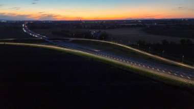 Piacenza Brescia karayolu kavşağında mavi saat boyunca akan A21 karayolu trafiği, araba ışık yolları ve şehir ışıkları akşam karanlığında hareket ve ulaşım kavramları yaratıyor.