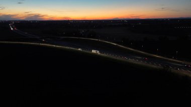 Gece hava görüntüsü A21 otoyolu Piacenza Brescia 'da gün batımında yoğun trafiği gösteriyor. Arabalar ve kamyonlar, farlarıyla yolu aydınlatıyor.