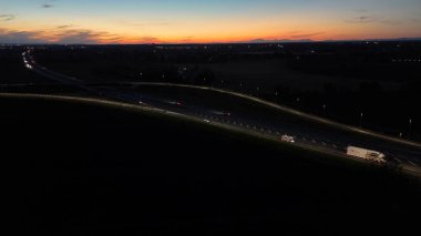 Gece hava görüntüsü A21 otoyolu Piacenza Brescia 'da gün batımında yoğun trafiği gösteriyor. Arabalar ve kamyonlar, farlarıyla yolu aydınlatıyor.