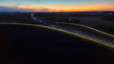 Piacenza Brescia karayolu kavşağında mavi saat boyunca akan A21 karayolu trafiği, araba ışık yolları ve şehir ışıkları akşam karanlığında hareket ve ulaşım kavramları yaratıyor.