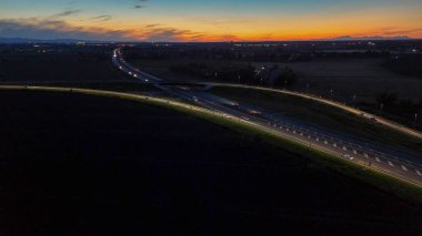 Piacenza Brescia karayolu kavşağında mavi saat boyunca akan A21 karayolu trafiği, araba ışık yolları ve şehir ışıkları akşam karanlığında hareket ve ulaşım kavramları yaratıyor.