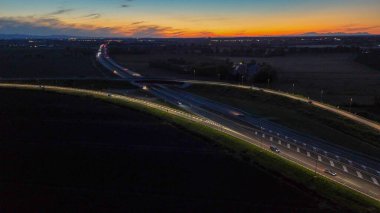 Piacenza Brescia karayolu kavşağında mavi saat boyunca akan A21 karayolu trafiği, araba ışık yolları ve şehir ışıkları akşam karanlığında hareket ve ulaşım kavramları yaratıyor.