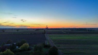 Günbatımında genişleyen Po Vadisi tarım alanlarının üzerine canlı renklerle gökyüzünü boyayarak, kırsal İtalya 'yı küresel kablosuz ağlara bağlayan önde gelen bir baz istasyonu yer alıyor.