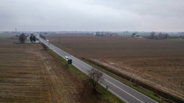 Piacenza, İtalya 26 Aralık 2025 'te İtalya' nın Castelvetro Piacentino kentindeki bir perakende satış merkezinin yakınında arabaları bulunan Strada Padana Inferiore S.S. 10 ile birlikte ekilmiş tarlalar.