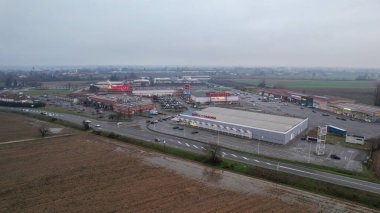 Piacenza, İtalya 26 Aralık 2025 'te birden fazla mağazası ve S.S. 10 Strada Padana Inferiore boyunca otoparkı olan ticari perakende merkezi işlek bir iş bölgesini gösteriyor.