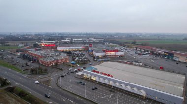 Piacenza, İtalya 26 Aralık 2025 Strada Padana Inferiore boyunca mağazaları, otoparkları ve çevresindeki kırsal bölgeleri olan büyük bir perakende merkezinin havadan görünüşü