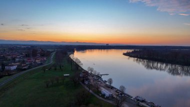 Po Nehri canlı günbatımı renklerini yansıtıyor. San Nazzaro 'yu bağlayan köprünün havadan görüntüsü. Monticelli d'Ongina. Emilia Romagna. İtalya. Kum çıkarma bölgesiyle. Mavnalar. Alacakaranlıkta geniş nehir manzarası