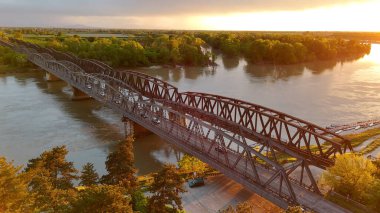 Demir Köprü 'nün günbatımında hava manzarası, Cremona, İtalya' da bir yol ve demiryolu viyadüğü, bir araba geçiyor ve altından Po Nehri akıyor.
