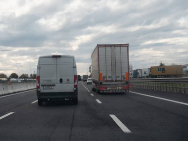 Yoğun bir otoyolda bulutlu bir gökyüzü ile giden araçlar günlük ulaşım ve ulaşım faaliyetlerini yakalıyor. Vicenza, İtalya - 21 Kasım 2025