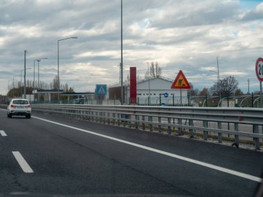 Bulutlu bir günde, yol çalışması işaretleriyle otoyolda giden bir araba bir seyahat ve ulaşım anını yakalıyor. Vicenza, İtalya - 21 Kasım 2025