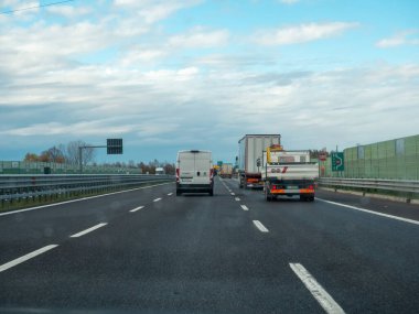 Yoğun bir otoyolda bulutlu bir gökyüzü ile giden araçlar günlük ulaşım ve seyahat anlarını yakalıyor. Vicenza, İtalya - 21 Kasım 2025