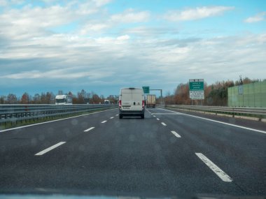 Bulutlu bir gökyüzü ile otoyolda giden araçlar günlük seyahat ve ulaşım anlarını yakalıyor. Vicenza, İtalya - 21 Kasım 2025