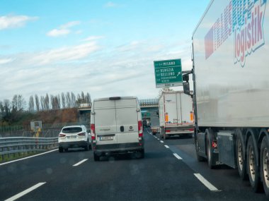 Yoğun bir otoyolda ilerleyen araçlar, önlerinde yön işaretleri, manzaralı bir yerde seyahat ve ulaşım anı yakalıyorlar. Vicenza, İtalya - 21 Kasım 2025
