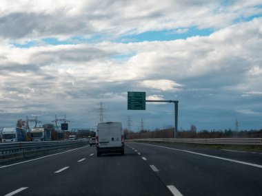 Tepesinde bulutlu bir gökyüzü olan otoyolda giden araçlar, hareket halindeki arabalar ve kamyonlarla tipik bir yol sahnesi gösteriyor. Vicenza, İtalya - 21 Kasım 2025
