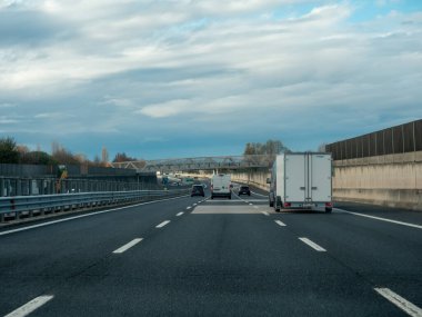 Yoğun bir otoyolda bulutlu bir gökyüzü ile giden araçlar hareket ve şehir yaşamını yakalıyor. Vicenza, İtalya - 21 Kasım 2025