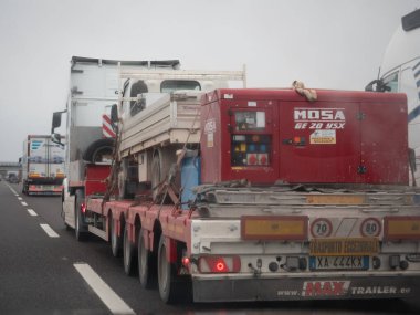 Büyük bir kamyon, yoğun bir otoyolda endüstriyel lojistik ve taşımacılık gösteren ağır makineler taşıyor. Vicenza, İtalya - 21 Kasım 2025
