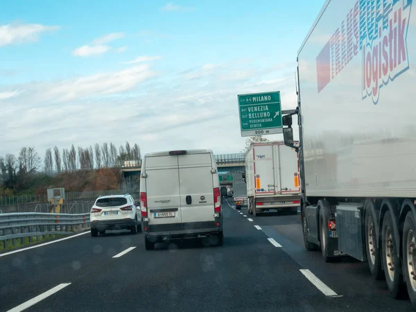 Yoğun bir otoyolda ilerleyen araçlar, önlerinde yön işaretleri, manzaralı bir yerde seyahat ve ulaşım anı yakalıyorlar. Vicenza, İtalya - 21 Kasım 2025