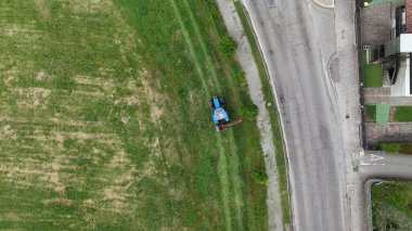 Küçük bir traktörün havadan görünüşü, özenle büyümüş otları ve uzun otları kesiyor şehir yolunun kenarında kentsel peyzaj bakımını ve kırsal mekaniği iş başında gösteriyor.