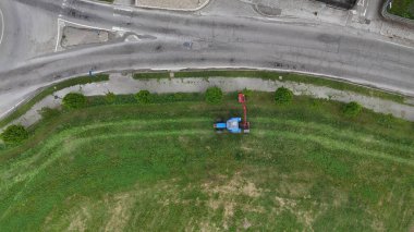 Hava görüntüsü, asfalt yola bitişik yemyeşil bir arazide çim biçen bir traktörü yakalıyor ve sakin kırsal bölgede güzel bir şekilde korunan bir manzara yaratıyor.
