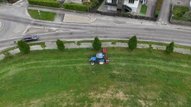 Tarım makinesi, kentsel bakım ve peyzaj bakımını gösteren hareketli ana caddenin yakınındaki bir kasaba çevresindeki otları ve otları özenle temizliyor.