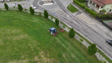 Tarım makineleri kentsel yeşil alanlara eğilimli aşırı gelişmiş otlar ve çimenler üzerinde çim biçme işlemleri yapan hareketli ana yol ve döner kavşak düzenli bir manzara yaratıyor