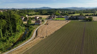 Tarım arazisi, açık mavi gökyüzünün altında traktörlerin tırmıklayıp saman balyalarını oluşturduğu kırsal hasat sezonunun özünü yakalıyor.